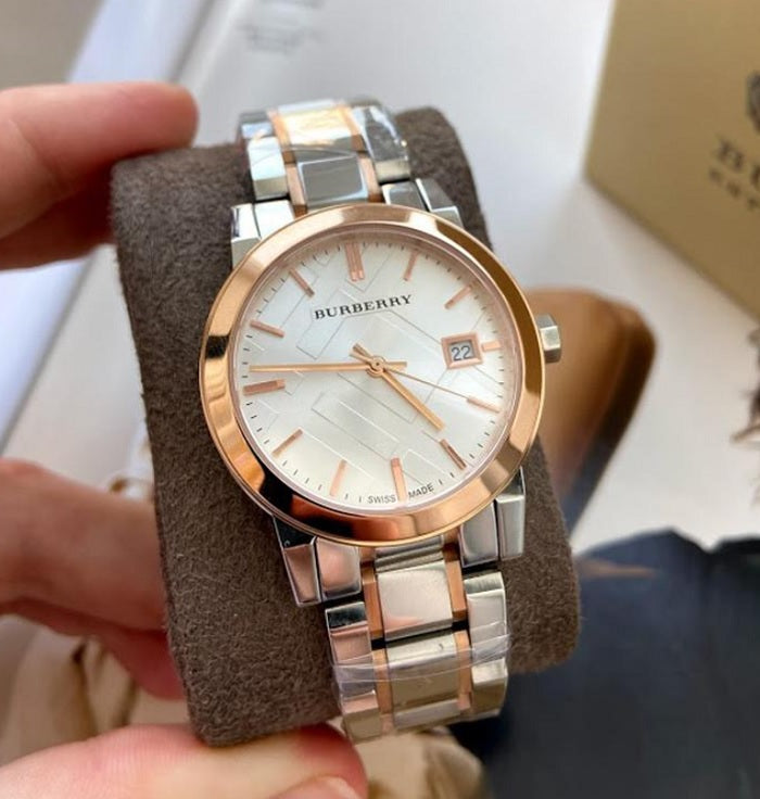 The Burberry BU9105 watch displayed on its original watch pillow, showing the silver and rose gold design.