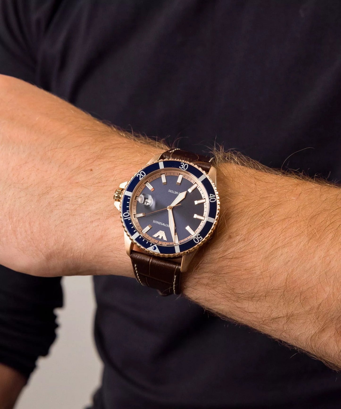 Emporio Armani AR11556 rose gold watch on men's wrist showing brown leather strap fit and blue dial contrast.