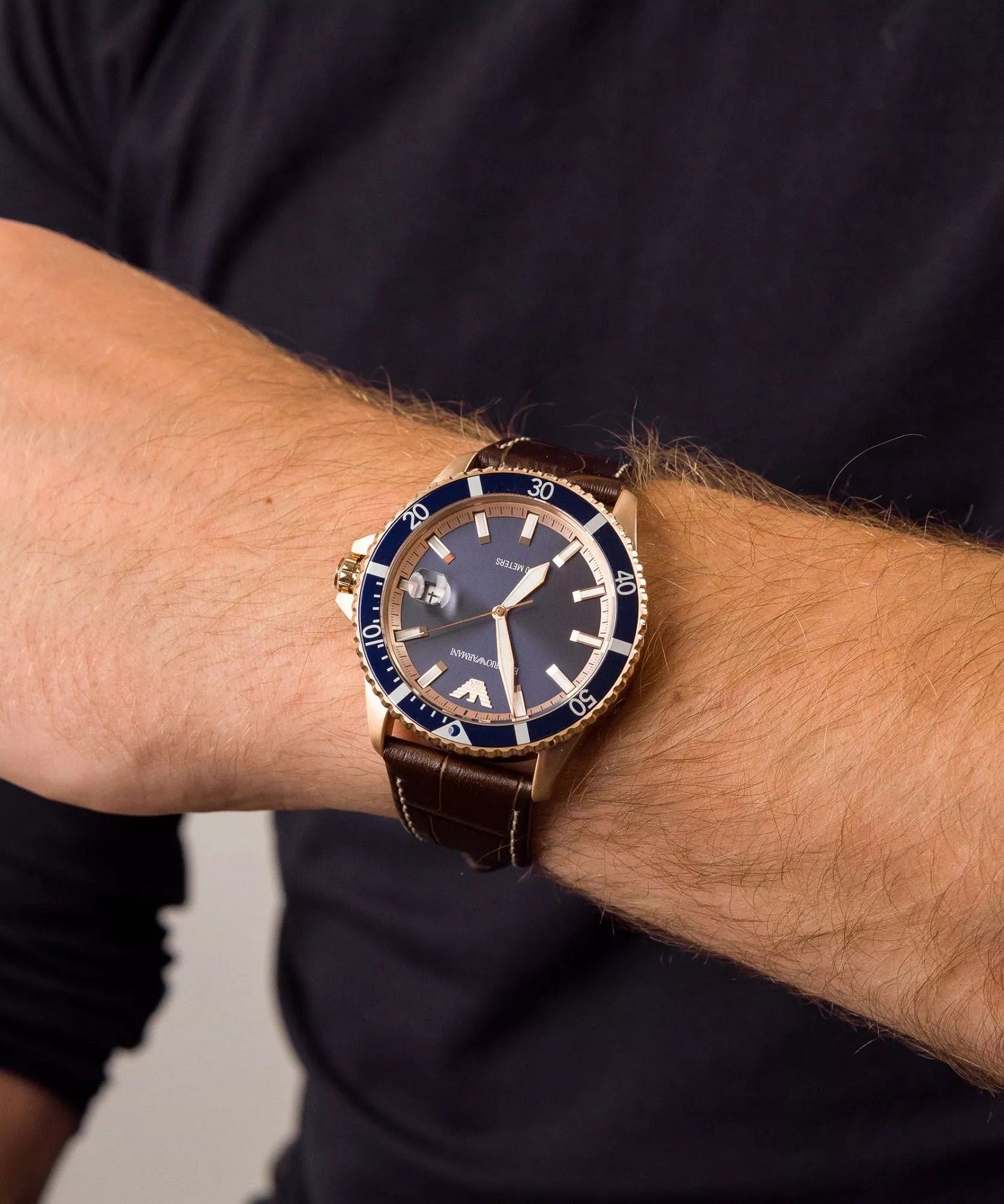 Emporio Armani AR11556 rose gold watch on men's wrist showing brown leather strap fit and blue dial contrast.