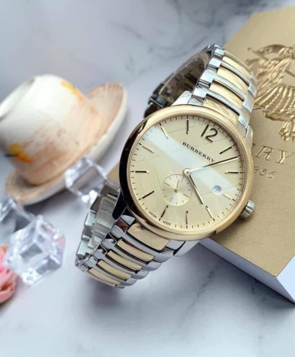 Burberry BU10011 men's two-tone watch displayed on a textured surface, highlighting its elegant gold dial and metallic finish.