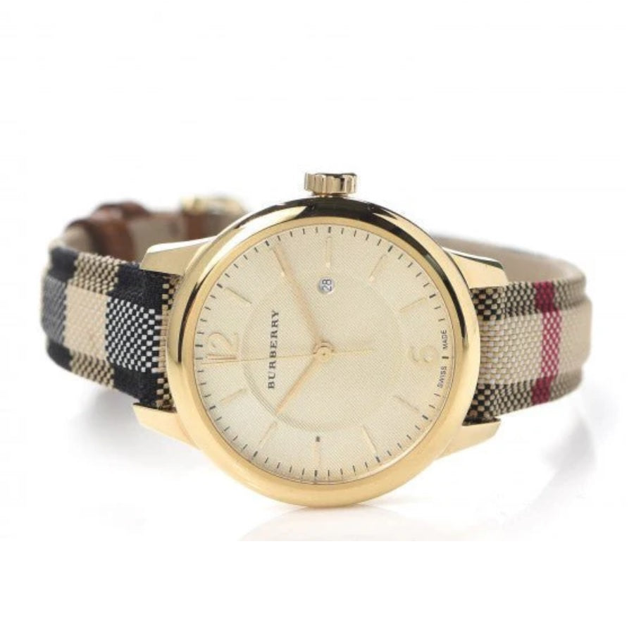 Angled view of the Burberry BU10104 showcasing the gold-tone case, clean dial with date window, and classic check pattern fabric strap.