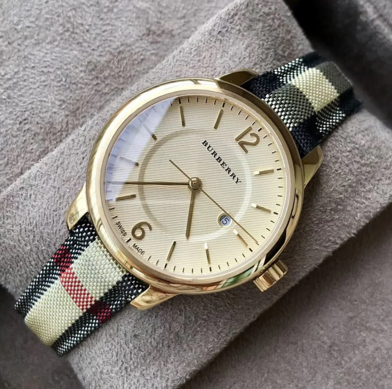 Burberry BU10104 classic gold watch resting on a soft grey surface, highlighting its elegant dial and iconic check strap.