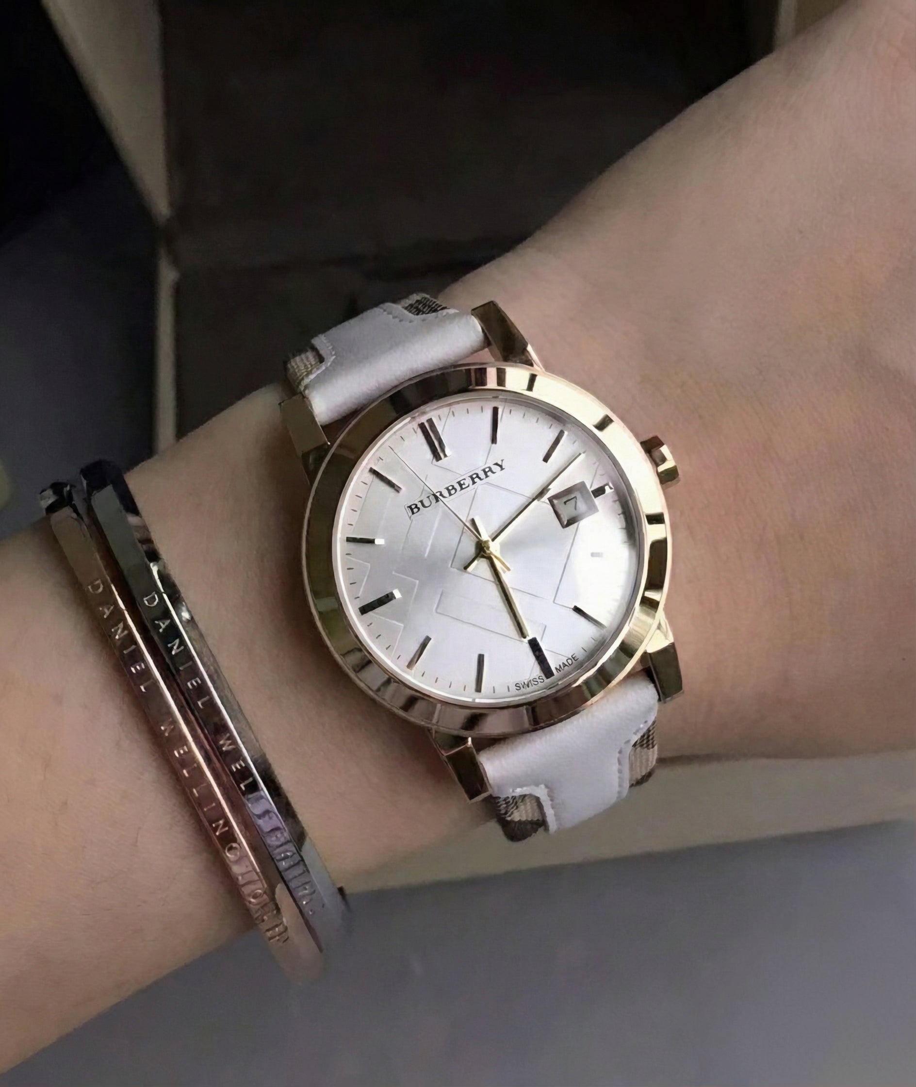 Woman wearing the Burberry BU9110 The City white leather watch on her wrist, styled with a bracelet to demonstrate everyday fit and sizing.