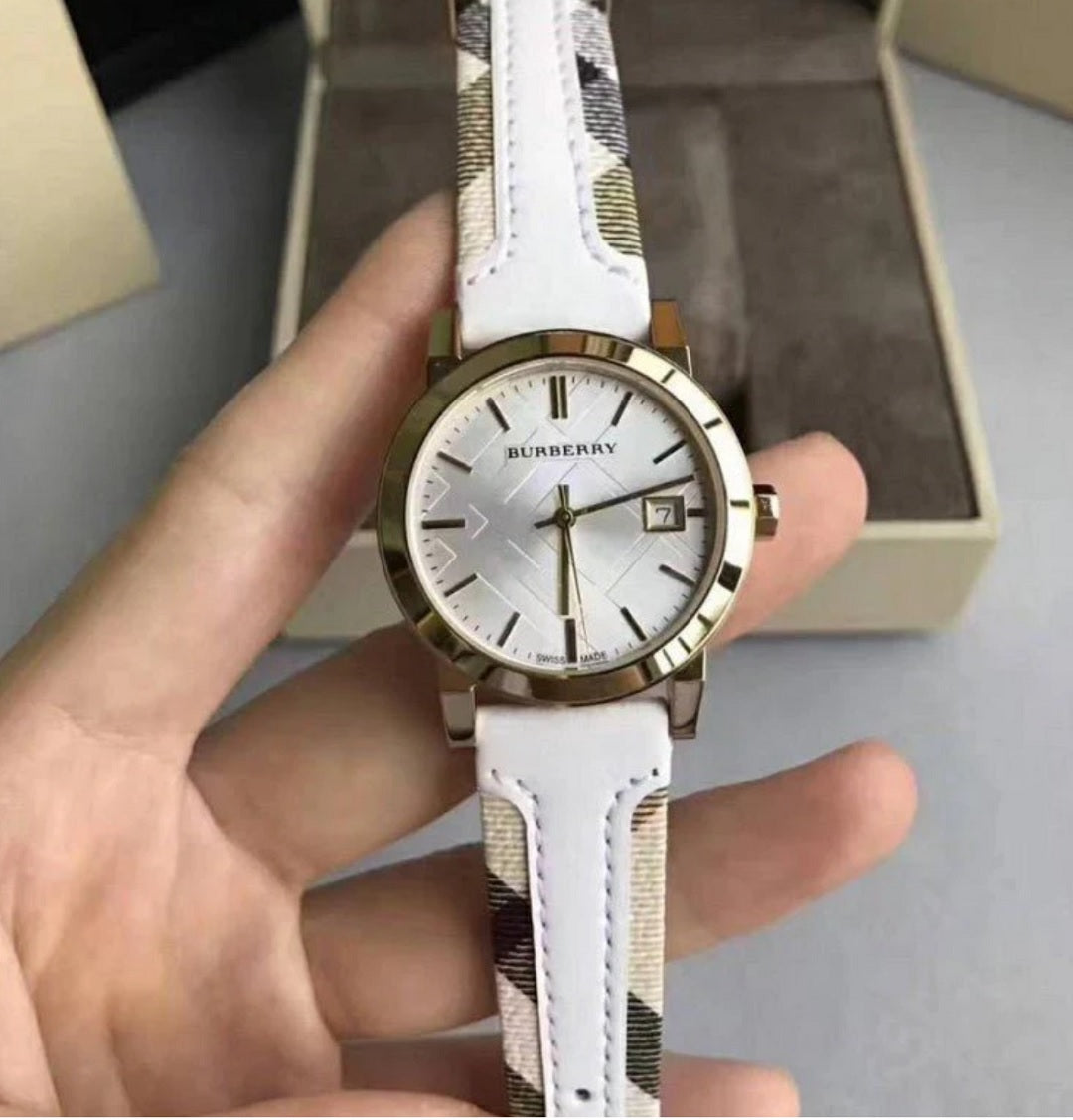 Hand holding the Burberry BU9110 white and gold watch, showcasing the dial and signature check fabric on the leather strap in natural lighting.