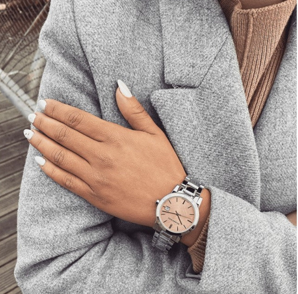 Woman wearing the Burberry BU9124 pink dial silver watch on her wrist, styled elegantly with a grey coat to demonstrate everyday wearability.