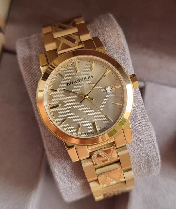 Burberry BU9145 women's gold watch resting on a soft display cushion, showcasing its polished metallic finish and intricate dial pattern.