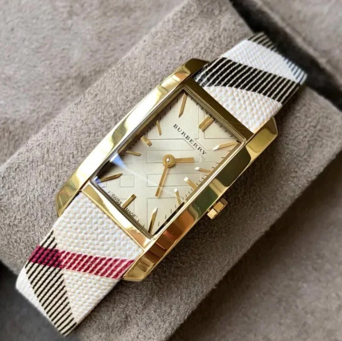 Burberry BU9509 rectangular gold watch resting on a soft textured surface, highlighting its classic beige check fabric strap.