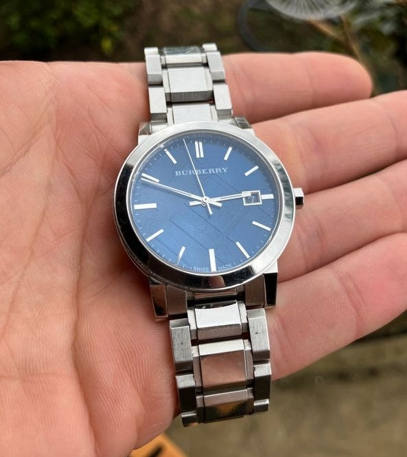 A Burberry BU9031 unisex watch with a silver-tone metal strap and a blue dial, and a date window.