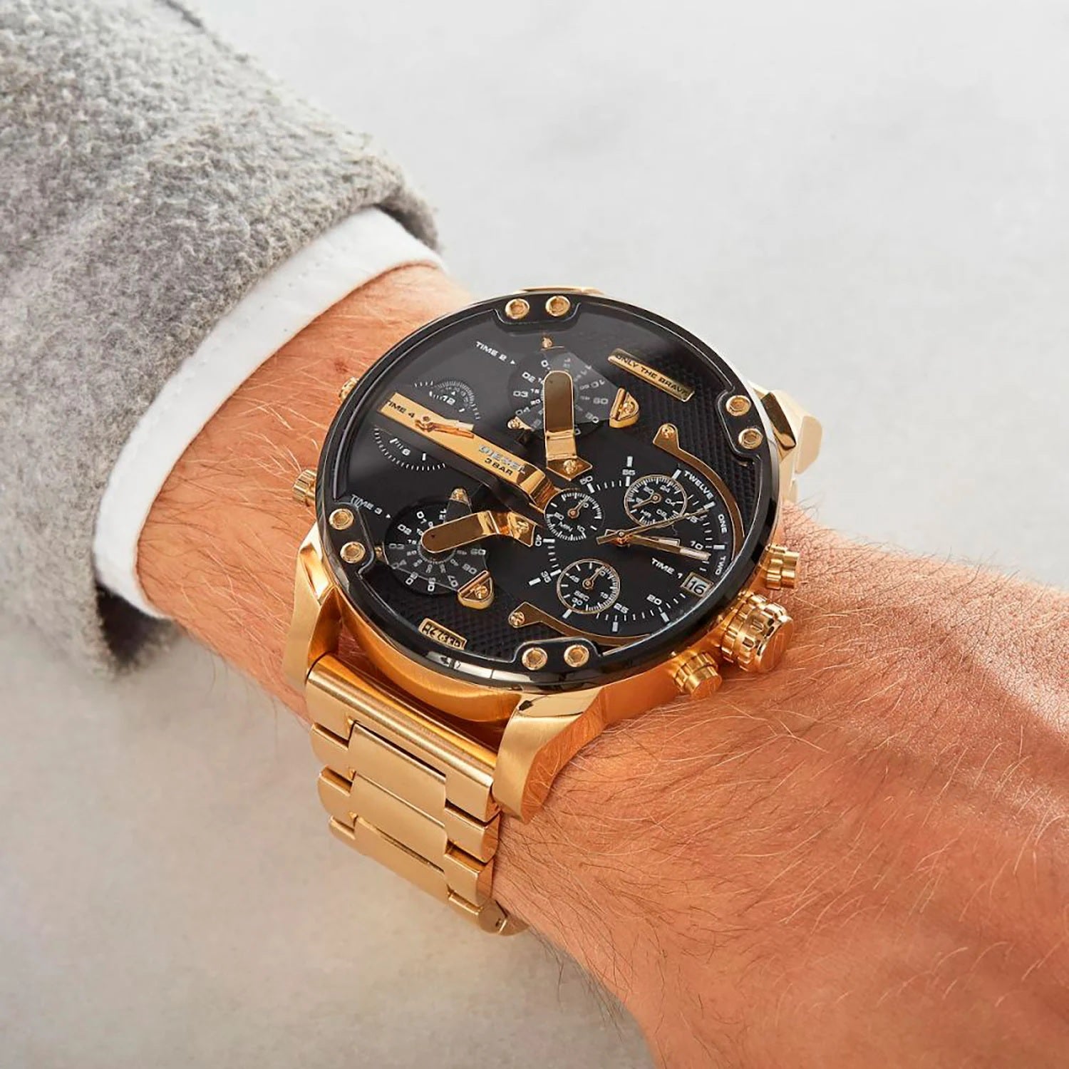 Man wearing the massive 57mm Diesel DZ7333 gold and black watch on his wrist, styled with a grey sleeve to demonstrate fit and bold streetwear styling.