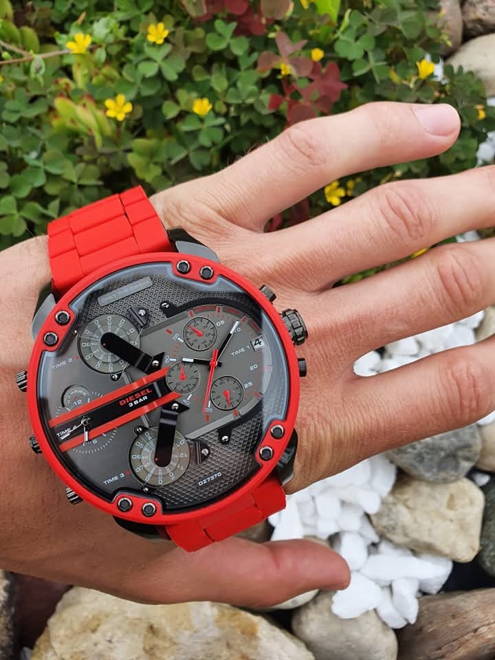 Hand holding the massive Diesel DZ7370 Mr. Daddy 2.0 red and gunmetal watch outdoors to demonstrate its scale and vibrant colour.