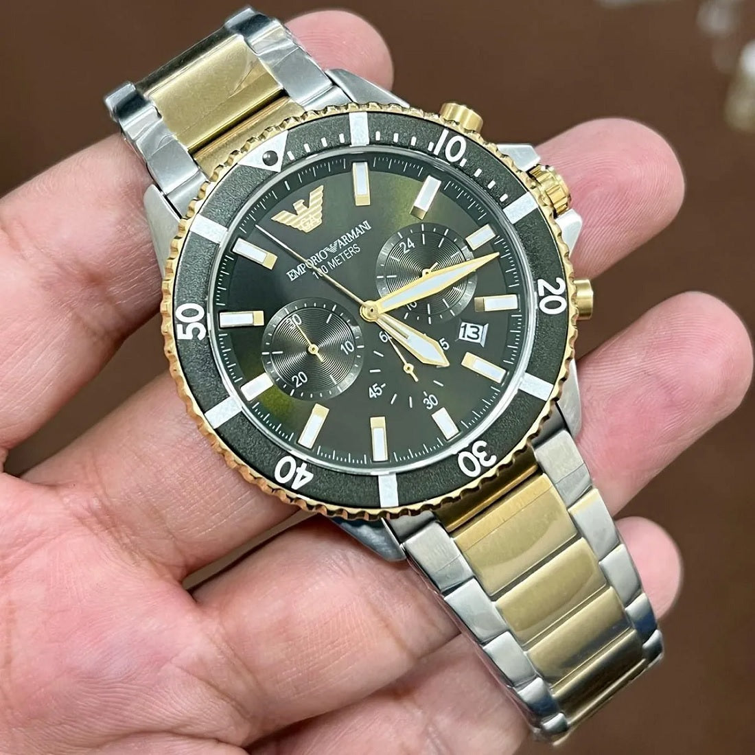Hand holding the Emporio Armani AR11361 green dial two-tone watch, demonstrating scale and metallic reflections in natural light.