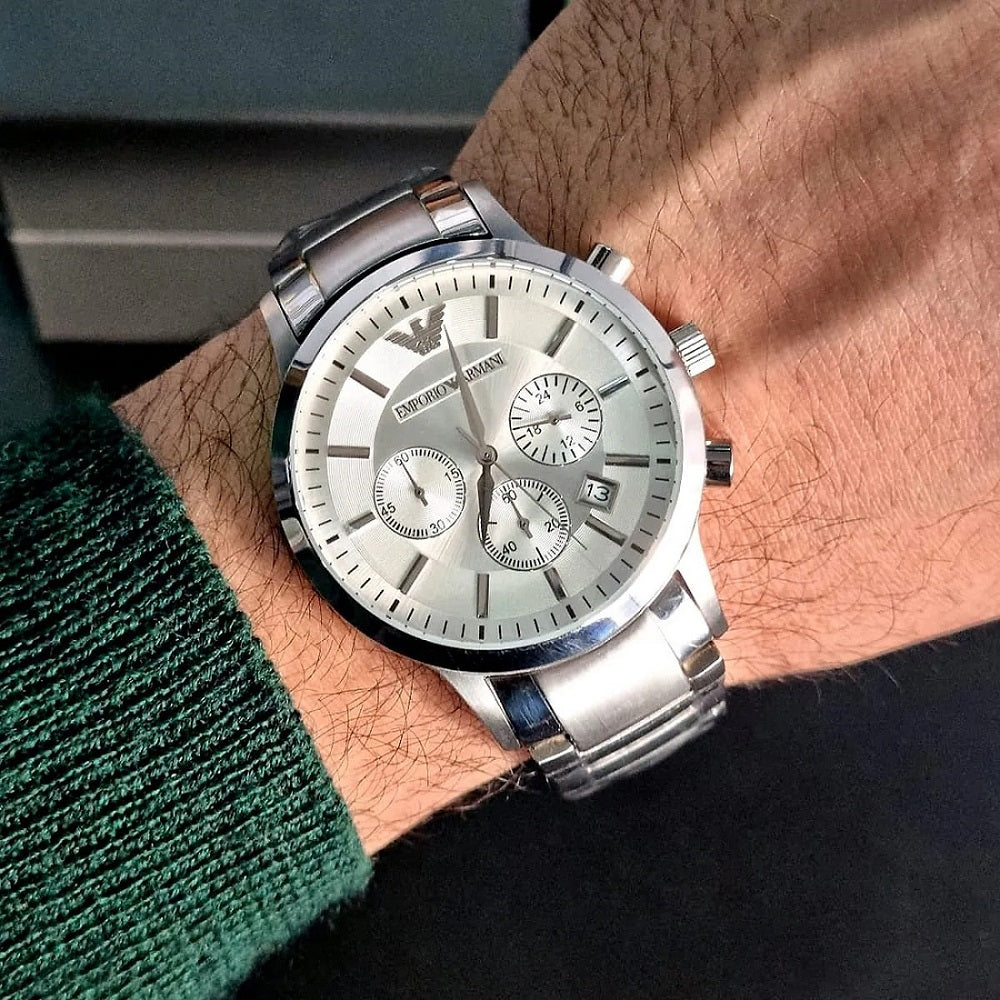 Lifestyle image of a man wearing the Emporio Armani AR2458 Renato silver watch on his wrist, styled with a green sweater to show everyday wearability.