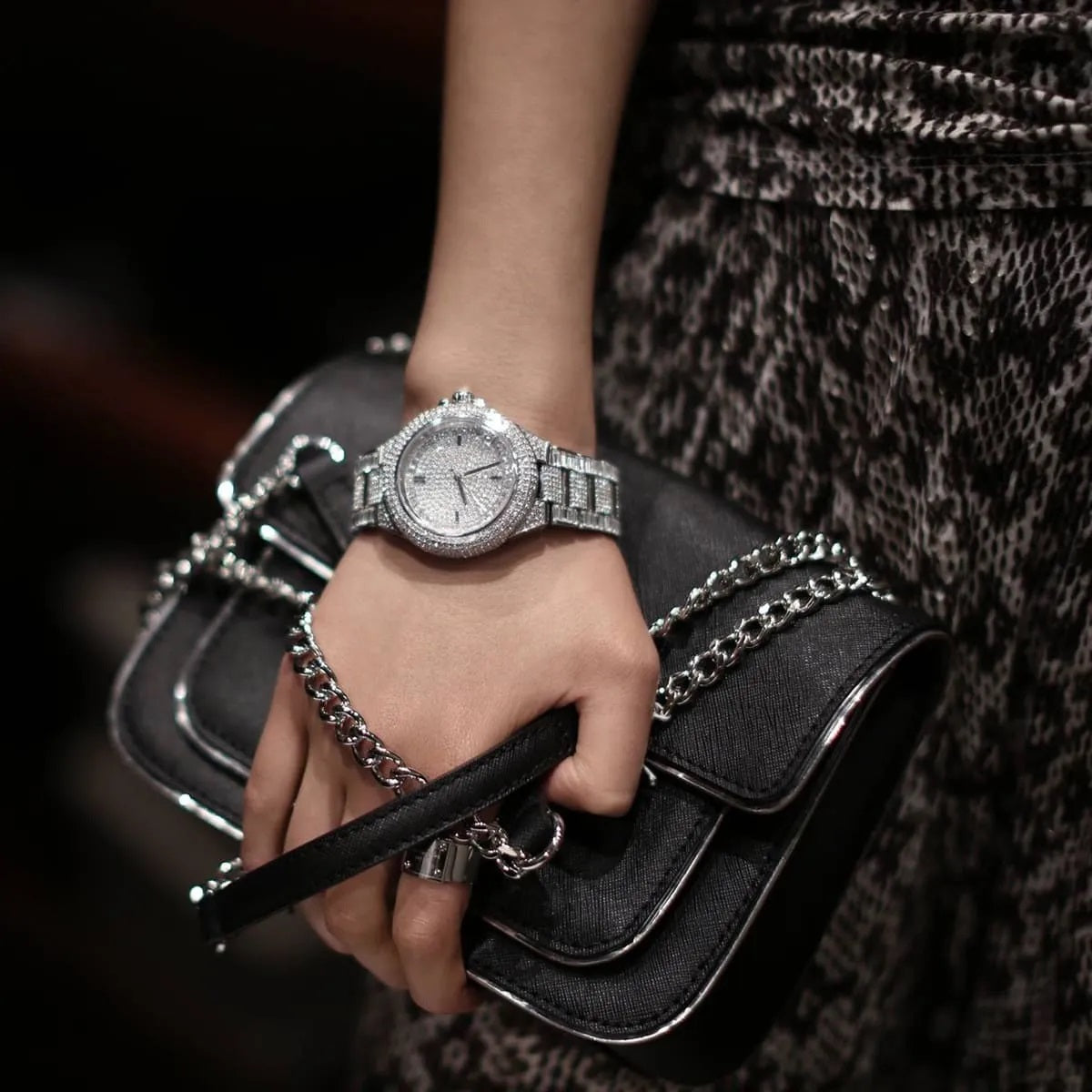 Lifestyle shot of a woman wearing the Michael Kors MK5869 silver crystal watch on her wrist, styled with a black designer handbag for a luxury look.