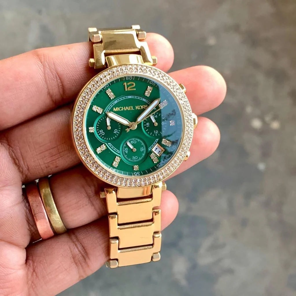 Hand holding the Michael Kors MK6263 women's watch in natural lighting to demonstrate scale, gold-tone finish, and vibrant green dial.
