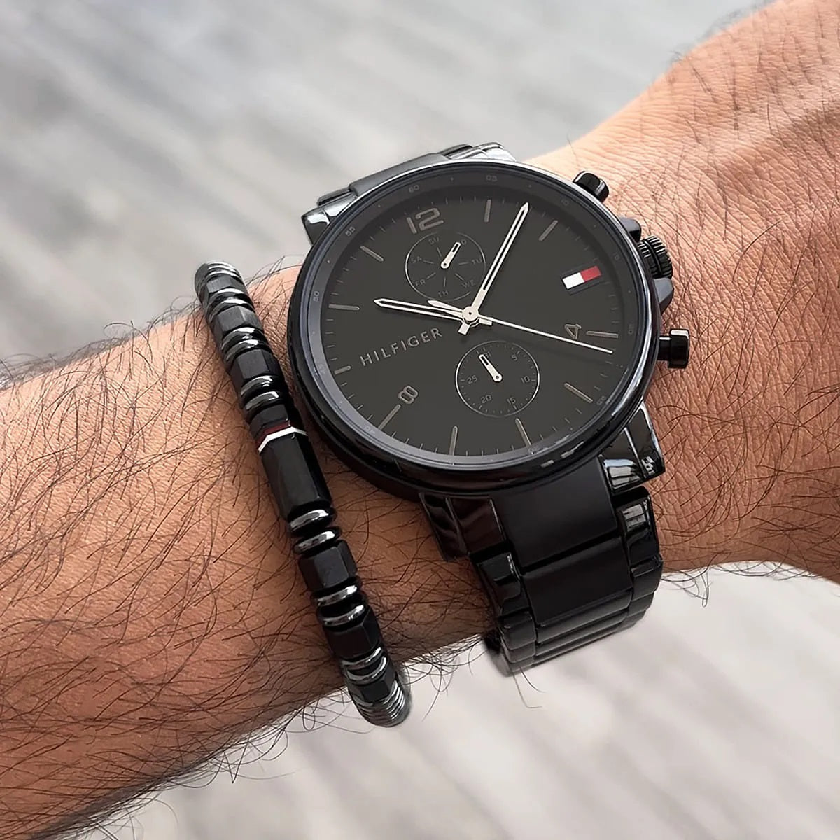Man wearing the Tommy Hilfiger 1710414 black watch on his wrist, styled with a beaded bracelet to demonstrate fit and everyday style.