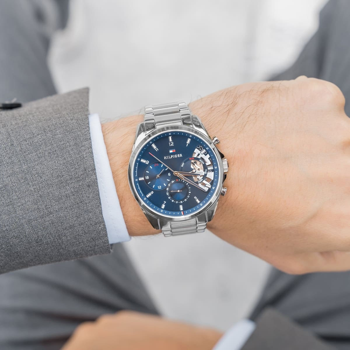 Professional styling of Tommy Hilfiger 1710448 Baker silver mesh watch worn with a charcoal grey jacket for a formal look.