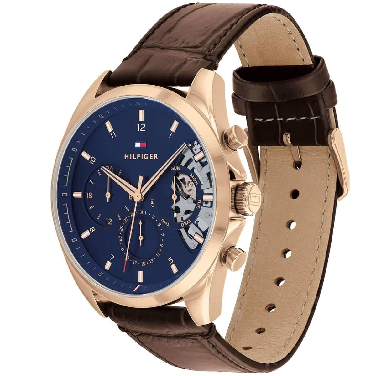 Angled view of the Tommy Hilfiger Baker watch showcasing the gold-tone case, blue multi-function dial, and textured leather strap.
