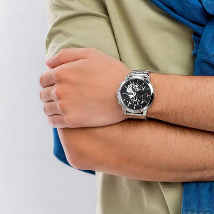 Lifestyle shot of the Tommy Hilfiger 1710477 Henry watch on a wrist, showcasing the industrial look of the black skeleton dial and silver bracelet.