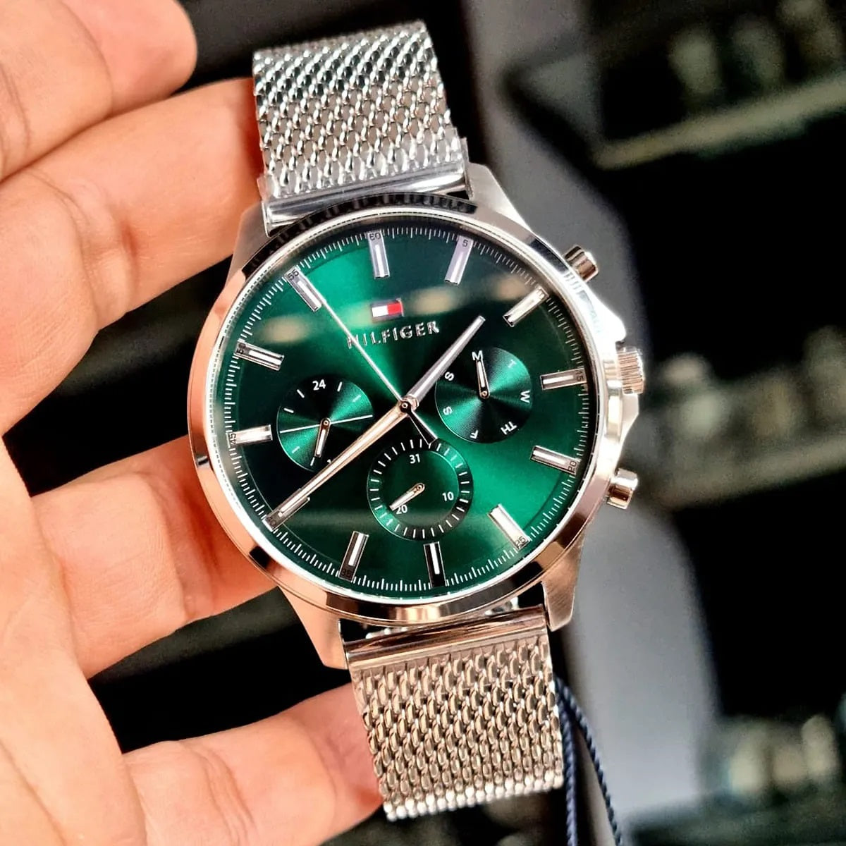 Handheld shot of the Tommy Hilfiger 1710499 Ryder watch capturing the reflective emerald green dial and silver mesh finish.