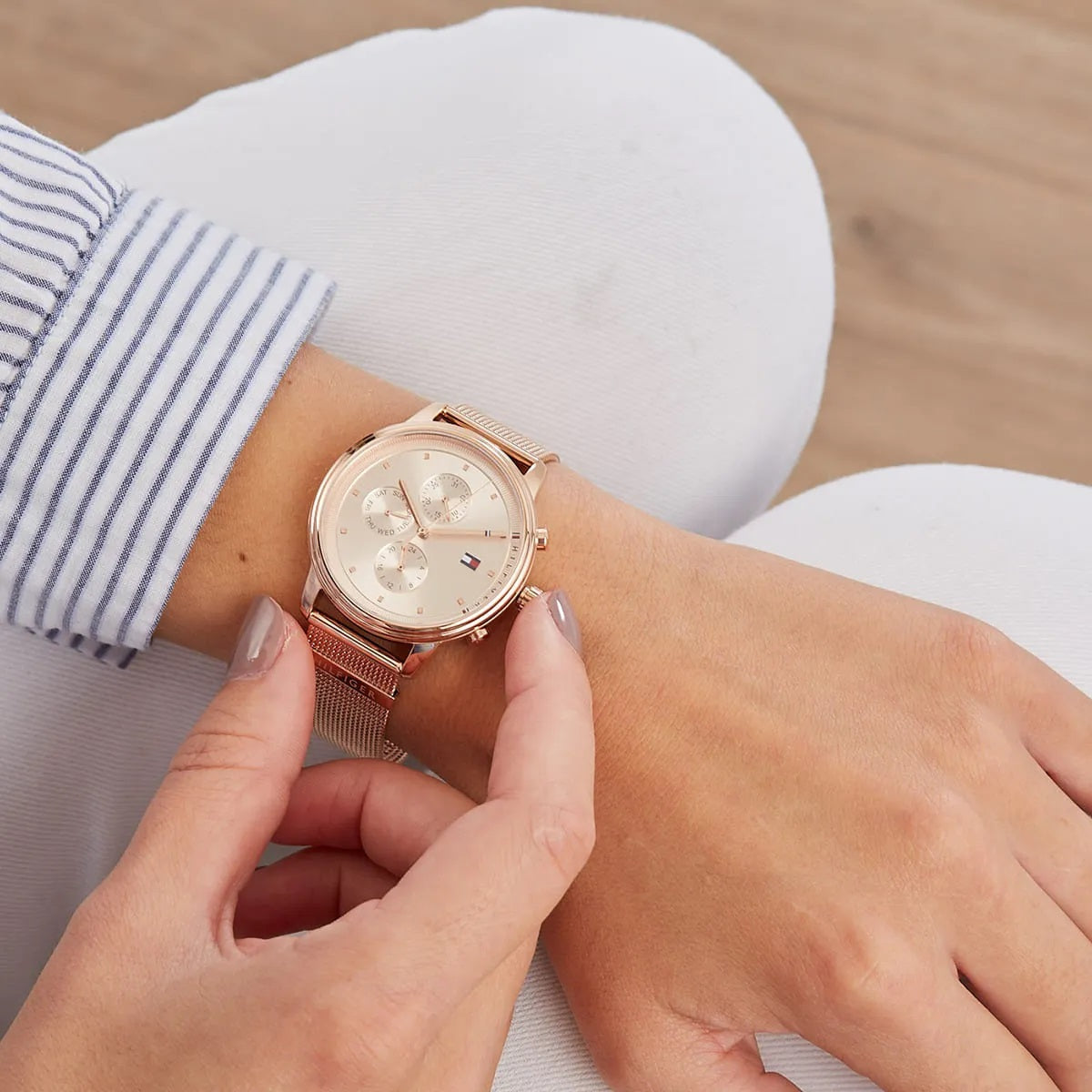 Woman wearing the Tommy Hilfiger 1781907 Blake rose gold watch on her wrist, styled with white trousers to show scale and elegance.