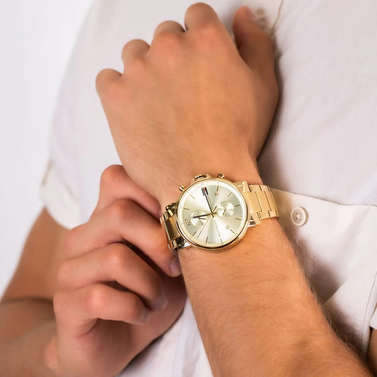 Lifestyle shot of a man wearing the Tommy Hilfiger Daniel gold watch on his wrist, styled with a white shirt to show size and fit.