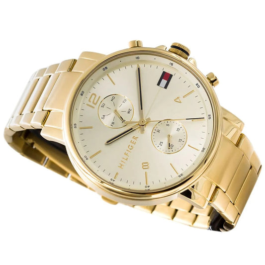Angled close-up of the Tommy Hilfiger Daniel watch showcasing the sunray gold dial, navy blue accents on the hands, and iconic flag logo.